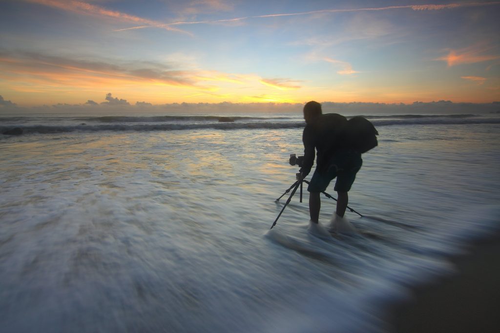 Travel photographer setting up tripod and camera in ocean.