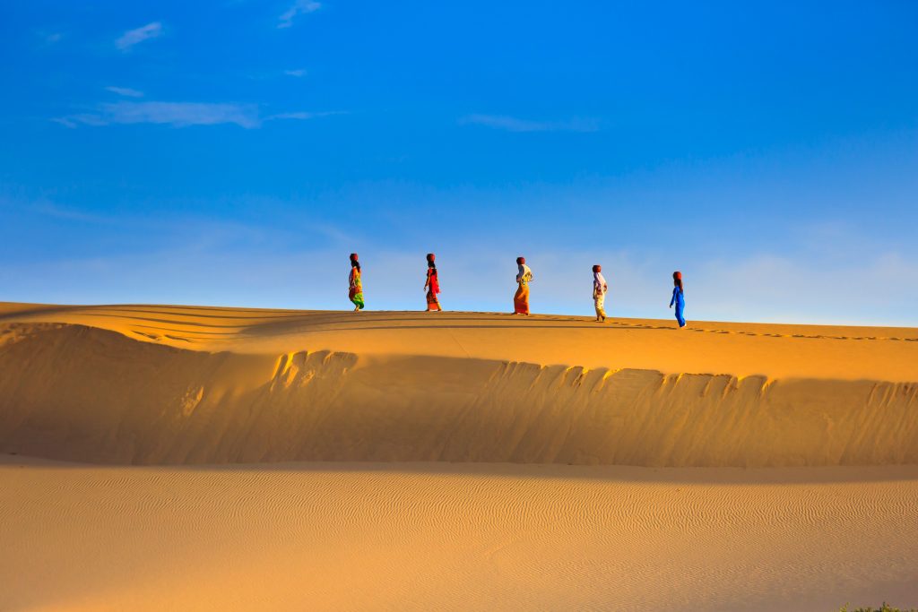 Women in colorful outfits walking in desert.