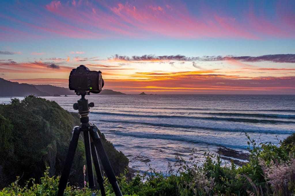 Camera on tripod on cliff looking out at ocean landscape during sunset