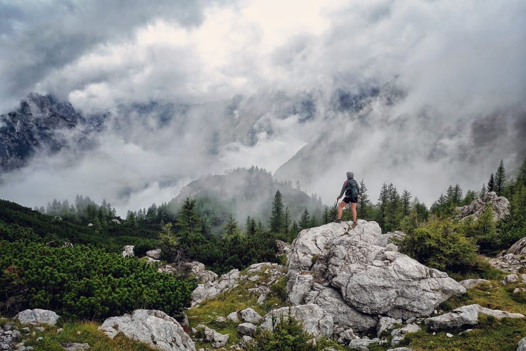 Landscape photograph with clouds rolling over mountains, a hiker in the forefront