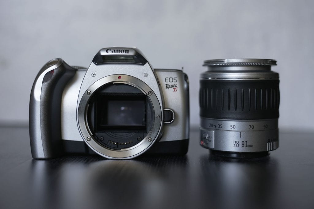 Silver Canon DSLR Camera with a silver zoom lens beside it
