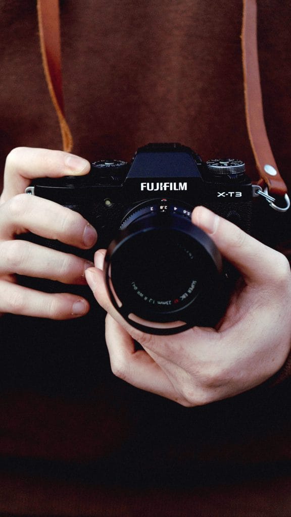 Person holding Fujifilm X-T3 camera in hands while wearing a brown leather camera strap around neck