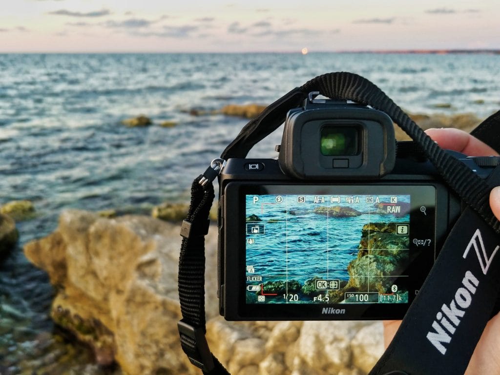 Nikon Z50 camera shown from behind being used to shoot a photo of the ocean