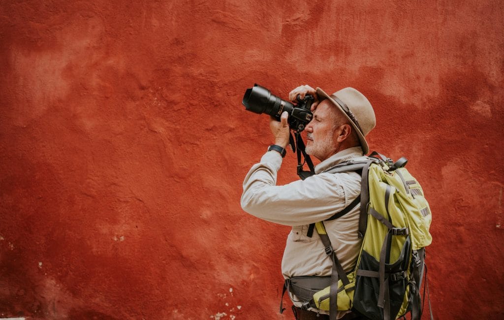 Man with backpack on taking picture with wildlife photography camera.