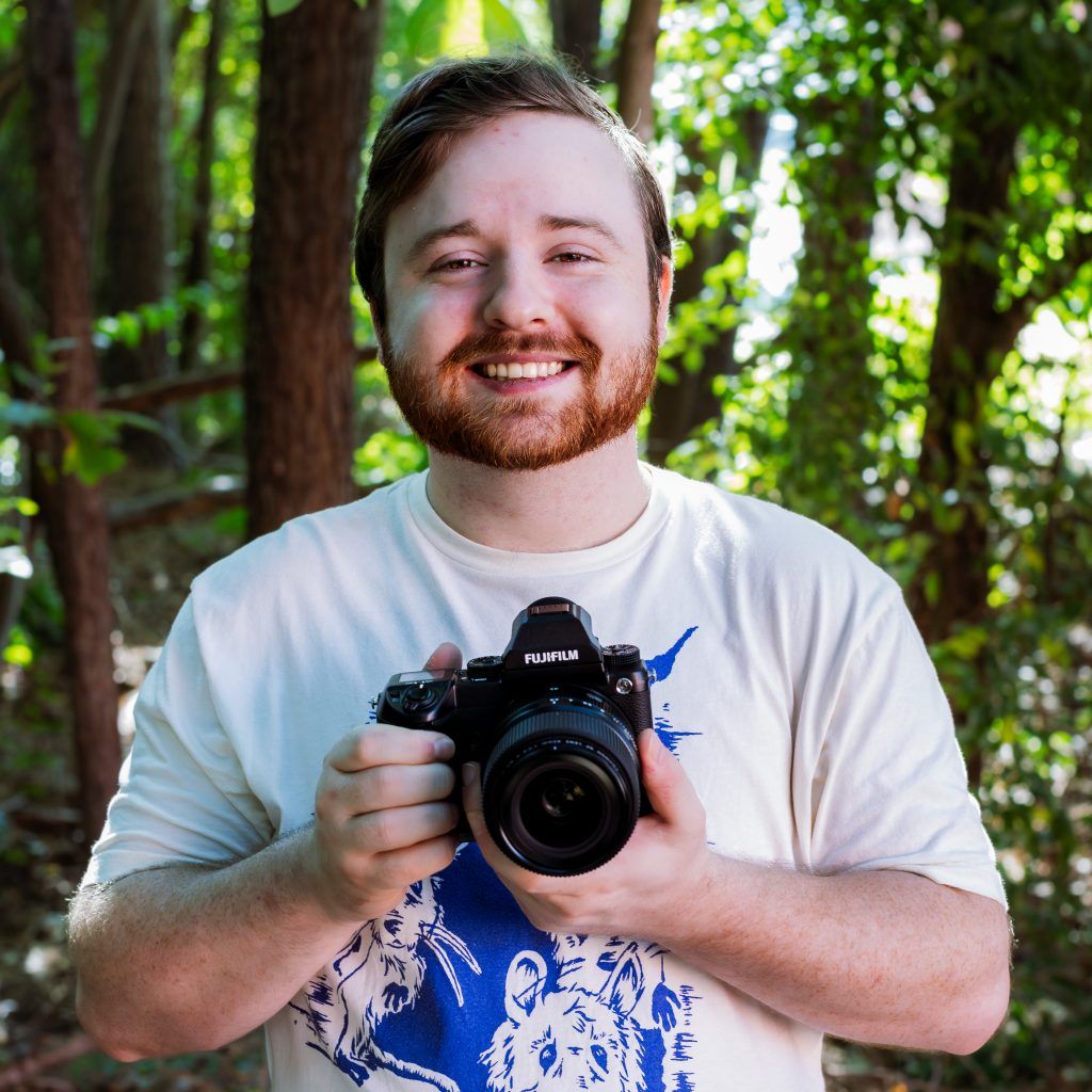 Photo of KEH staff member Jake holding his Fujifilm GFX 50S camera and smiling.