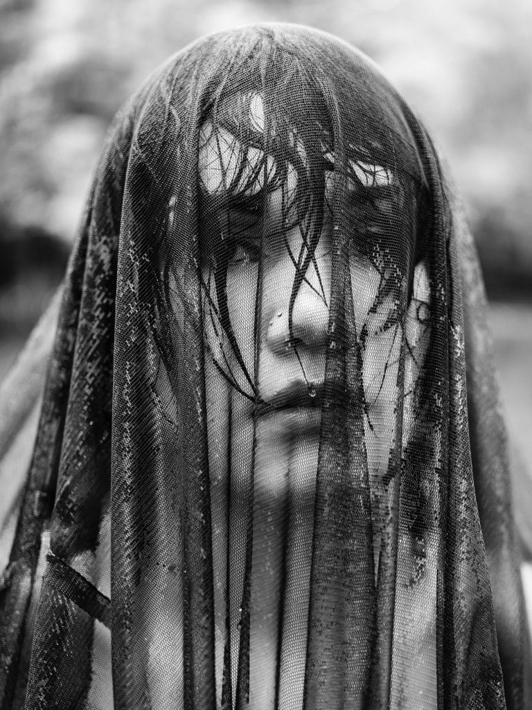 Black and white portrait of a woman under a wet black veil.